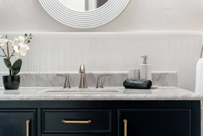 Elegant vanity with marble countertop, brushed nickel fixtures, and a navy cabinet accented by gold hardware. A fresh orchid and modern details add a touch of luxury to this serene bathroom space.