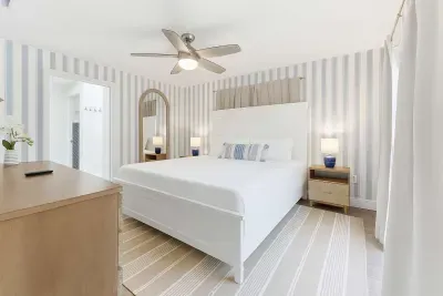Serene primary bedroom featuring soft striped walls, a plush king bed, and coastal-inspired accents. Bright and airy with a soothing palette—perfect for unwinding after sun-filled days in comfort and style.