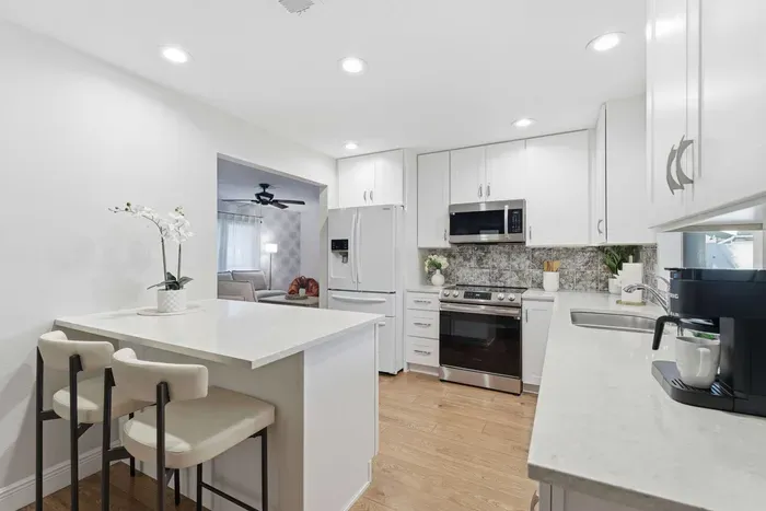 Bright and modern kitchen featuring sleek white cabinetry, stainless steel appliances, and a cozy breakfast bar. Perfectly equipped for home-cooked meals or morning coffee, blending style and functionality in every detail.