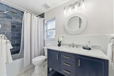 Chic bathroom with navy cabinetry, marble countertop, and bold subway tile shower. Elegant lighting and soft touches create a fresh, spa-like atmosphere perfect for relaxation.