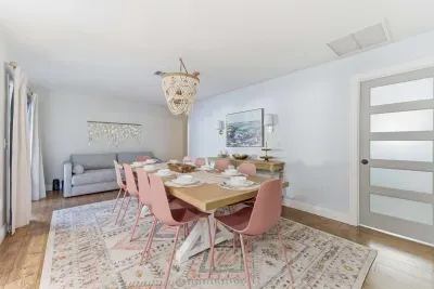 Bright and inviting dining space featuring blush pink chairs, a stylish wooden table, and a soft patterned rug. Perfect for group dinners or morning coffee, this airy room blends modern charm with cozy elegance for memorable gatherings.