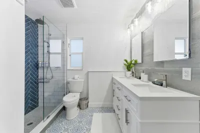 Elegant bathroom with a double vanity, striking blue herringbone shower, and patterned tile floor. Bright lighting and modern finishes create a fresh, spa-like retreat for your stay.