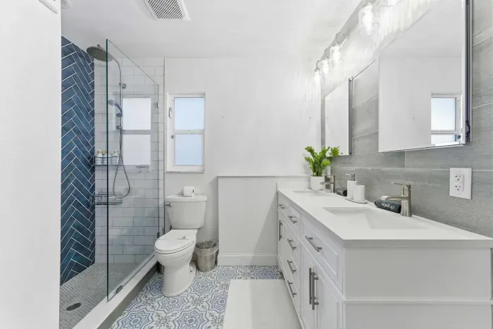 Elegant bathroom with a double vanity, striking blue herringbone shower, and patterned tile floor. Bright lighting and modern finishes create a fresh, spa-like retreat for your stay.