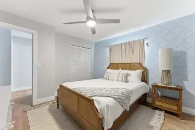 Inviting bedroom with a cozy wooden bed frame, soft neutral tones, and elegant patterned wallpaper. A serene and stylish retreat designed for restful nights and peaceful mornings.
