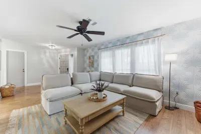 Bright and airy living room with a cozy sectional, stylish wallpaper, and soft natural light. Perfect for relaxing after a beach day or movie nights in comfort—this inviting space blends modern charm with laid-back coastal vibes.