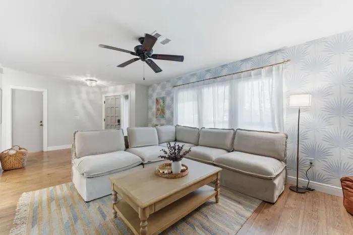 Bright and airy living room with a cozy sectional, stylish wallpaper, and soft natural light. Perfect for relaxing after a beach day or movie nights in comfort—this inviting space blends modern charm with laid-back coastal vibes.