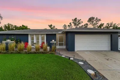 Beautiful modern home with sleek blue exterior, lush green lawn, and vibrant landscaping. Welcoming curb appeal sets the tone for a stylish and relaxing coastal getaway.