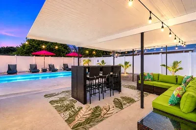 Covered outdoor bar with seating for five, sectional big enough for the whole group, and a poolside view - this is where the adults settle in while the kids stay in the pool.