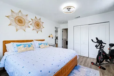 King bed under two woven sunbursts, Schwinn IC4 in the corner — the master handles both ends of the day.