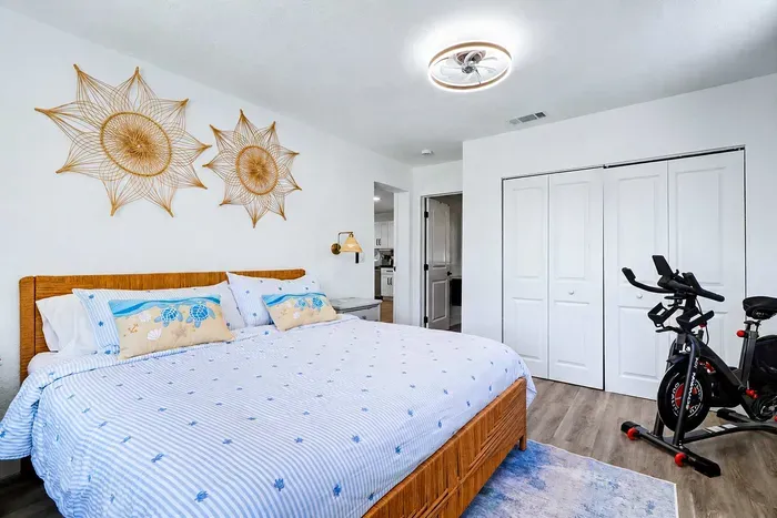 King bed under two woven sunbursts, Schwinn IC4 in the corner — the master handles both ends of the day.