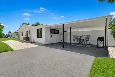 Propane grill under the covered carport, four-seat bistro table, and a fence gate straight to the pool — grill the food, walk it through, eat by the water.