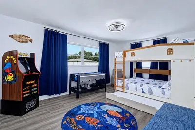 Arcade1Up PAC-MAN in the corner, four-game combo table by the window, boat bunk bed with pull-out trundle — this is the room the kids claim before the bags are unpacked.