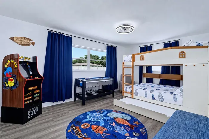 Arcade1Up PAC-MAN in the corner, four-game combo table by the window, boat bunk bed with pull-out trundle — this is the room the kids claim before the bags are unpacked.