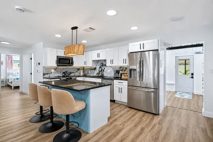 Renovated kitchen with full stainless suite, marble backsplash, and a three-seat island — the family cooks together, eats together, and heads out to the pool from the same room.