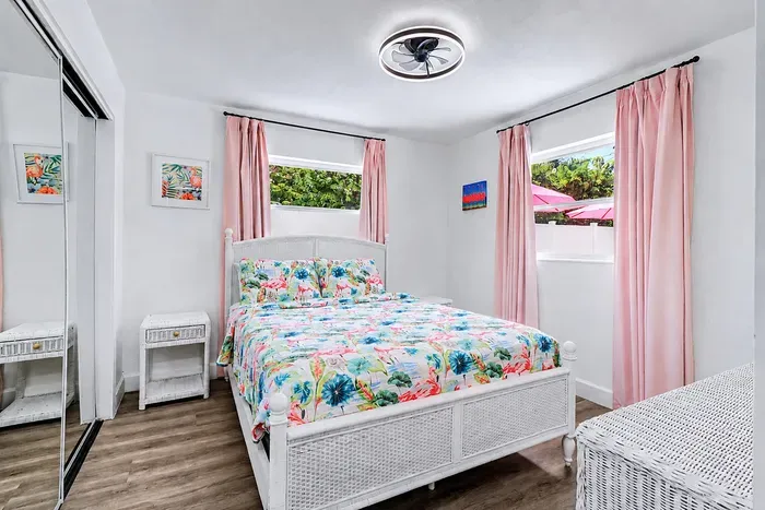 White wicker bed frame, flamingo florals, pink curtains, pool-view window — someone in the group is going to call dibs on this room before the bags are unpacked.