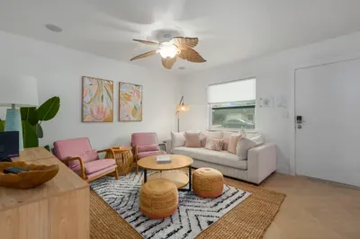 Spacious, sunlit living room with cozy seating, coastal textures, and stylish accents. Unwind under the ceiling fan, enjoy movie nights, or gather with friends in this welcoming space designed for comfort, conversation, and relaxation.
