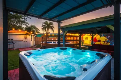 Soak after dark in this glowing hot tub oasis under a covered patio. Ambient lighting, tropical palms, and vibrant mural vibes set the mood—perfect for evening relaxation, late-night laughs, and unforgettable vacation moments.