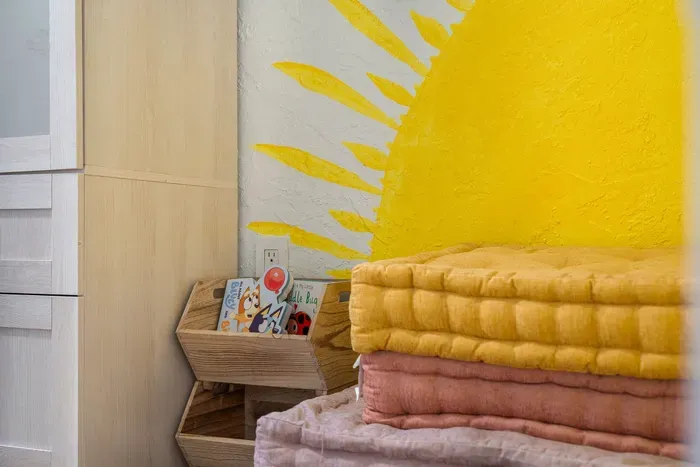 Thoughtful bedroom touches with soft folded linens, cozy textures, and a cheerful sunburst mural. Warm, welcoming details create a playful yet relaxing vibe—perfect for unwinding and feeling right at home.