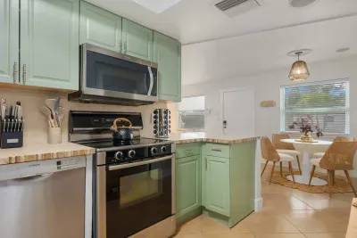 Bright, coastal kitchen with soft green cabinetry, stainless appliances, and spacious counters. Cook with ease, enjoy morning coffee, and gather nearby in the sunny dining nook—perfect for relaxed meals and beachy living.