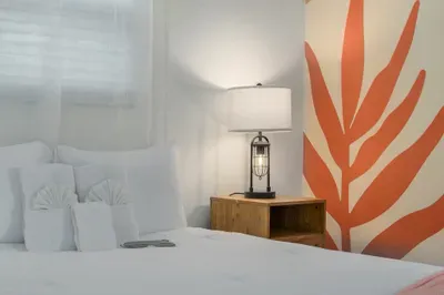 Cozy bedroom details with plush white linens, warm wood nightstand, and soft bedside lighting. Bold tropical mural accents add personality, creating a calm, stylish retreat perfect for restful nights and relaxed mornings.