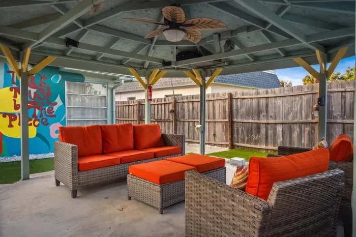 Spacious covered outdoor lounge with plush seating, bold cushions, and a breezy ceiling fan. Perfect for relaxing after a swim, enjoying cocktails with friends, or unwinding in the shade with vibrant, beachy vibes all around.