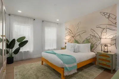 Tranquil bedroom retreat with plush bedding, soft lighting, and a beautiful tropical mural backdrop. Natural light, calming tones, and cozy textures create a peaceful space to unwind and recharge after beach-filled days.