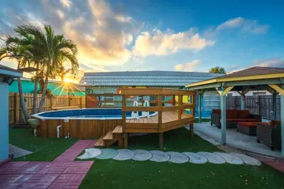 Spacious backyard retreat with private pool, elevated deck, hot tub, and covered lounge. Tropical palms, sunset views, and vibrant murals create the ultimate space for swimming, soaking, grilling, and unforgettable outdoor memories.