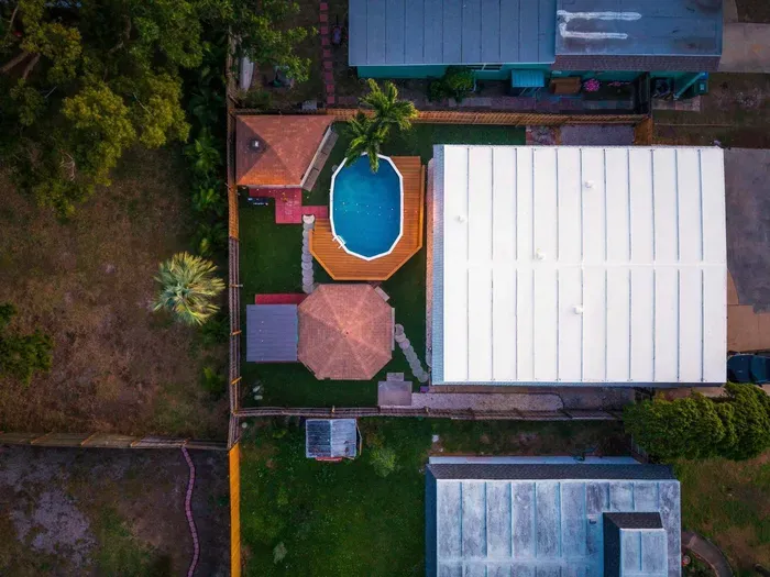 Aerial view of your private backyard oasis featuring a sparkling pool, hot tub, covered lounge, and dining areas. Fully fenced and thoughtfully laid out, this tropical retreat is perfect for relaxing, entertaining, and unforgettable vacation memories