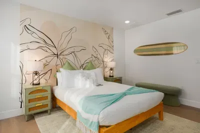Relax in this stylish tropical bedroom featuring plush bedding, serene mural accents, and warm coastal décor. Soft lighting and calming tones create the perfect retreat for restful nights and slow, refreshing mornings.