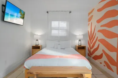 Bright, tropical bedroom with plush bedding, bold mural accent, and soft natural light. Unwind with your favorite show, enjoy cozy nights, and wake refreshed in this stylish, beach-inspired retreat.
