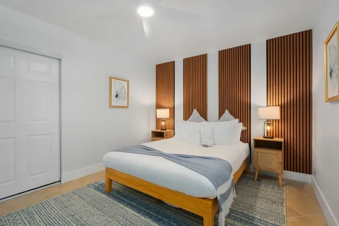 Calm and modern bedroom with plush bedding, warm wood panel accents, and soft ambient lighting. Designed for comfort and tranquility, this inviting space is perfect for restful nights and slow, relaxing mornings.