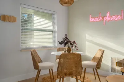 Charming dining nook with coastal flair, rattan seating, and playful “beach please” neon sign. Sunlit and stylish, it’s the perfect spot for morning coffee, casual meals, or planning your next sunny adventure.