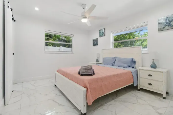Relax in this comfortable bedroom featuring a double-sized bed, perfect for a restful night’s sleep. The room is filled with natural light from two large windows, creating a bright and airy ambiance.