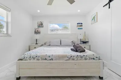 Enjoy a restful stay in this inviting bedroom featuring a plush queen-sized bed, framed by two windows that fill the space with natural light. Two small side tables add both charm and functionality. A comfortable and relaxing space to unwind.