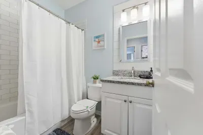 Bright and clean bathroom featuring granite countertops, coastal blue walls, and a fresh white shower. Modern and inviting, it’s the perfect space to refresh and unwind after a day in the sun.