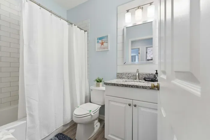 Bright and clean bathroom featuring granite countertops, coastal blue walls, and a fresh white shower. Modern and inviting, it’s the perfect space to refresh and unwind after a day in the sun.