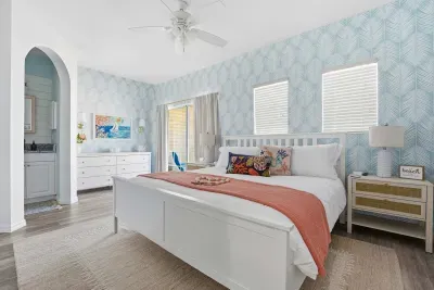Serene coastal bedroom with a king bed, ocean-inspired wallpaper, and soft coral accents. Cozy lighting and beachy details create a peaceful space to unwind and drift off to the sound of nearby waves.