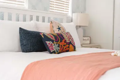 Featuring crisp white linens, a soft coral throw, and vibrant accent pillows that add a splash of seaside color. Bathed in natural light, this peaceful retreat invites restful sleep and slow, relaxing mornings.