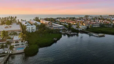 Stunning aerial sunset view over tranquil coastal waters and charming beachside homes. A peaceful setting that perfectly captures the relaxed beauty of island living.