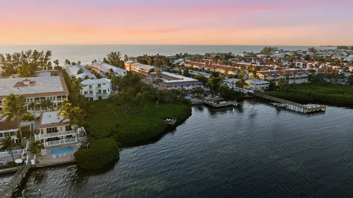 Stunning aerial sunset view over tranquil coastal waters and charming beachside homes. A peaceful setting that perfectly captures the relaxed beauty of island living.