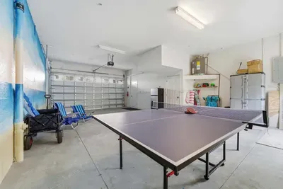Spacious garage game room featuring a ping pong table, beach gear, and plenty of storage. Perfect for family fun, friendly matches, or grabbing essentials for a day by the ocean.