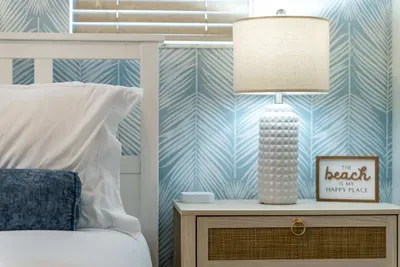 Cozy bedside setup with soft coastal lighting, textured wallpaper, and beach-inspired décor. The warm glow and soothing colors create the perfect spot to unwind and drift into seaside serenity.