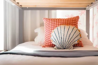 Adorable coastal bunk retreat full of charm and comfort. Featuring crisp white linens, a soft gray throw, and playful seaside accent pillows, this cozy nook is perfect for kids or extra guests.