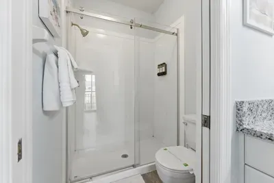 Modern bathroom with a sleek glass shower, granite counters, and crisp white finishes. Bright, clean, and refreshing—perfect for rinsing off after a sunny day at the beach.