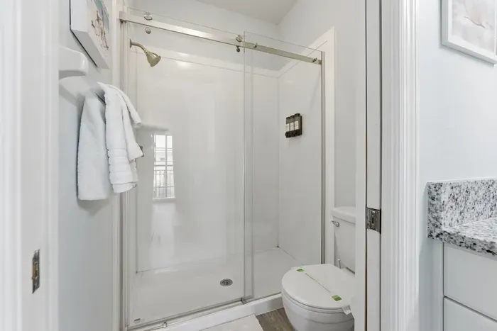 Modern bathroom with a sleek glass shower, granite counters, and crisp white finishes. Bright, clean, and refreshing—perfect for rinsing off after a sunny day at the beach.