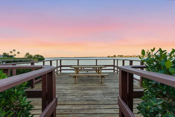 Scenic boardwalk leading to a peaceful waterfront deck with sunset views. Enjoy dining, relaxing, or simply watching the sky glow over calm coastal waters.