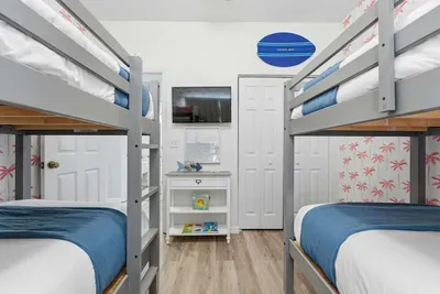 Fun and inviting bunk room featuring two twin-over-twin beds, a TV, and playful beach décor. Perfect for kids or friends, this bright space offers comfort and coastal charm for a memorable stay.