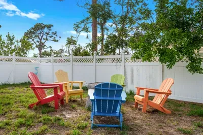 Unwind in this colorful outdoor space featuring a cozy firepit surrounded by bold, bright Adirondack chairs.
