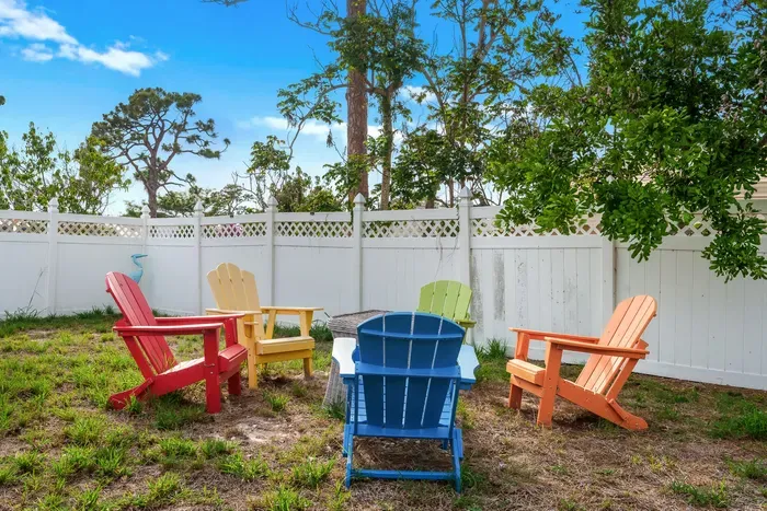 Unwind in this colorful outdoor space featuring a cozy firepit surrounded by bold, bright Adirondack chairs.