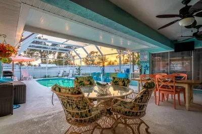 Dine in tropical comfort with this stylish indoor-outdoor patio area, featuring a glass-top rattan dining set and vibrant decor.